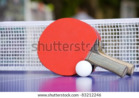 Two table tennis or ping pong rackets and balls on a blue table with net; shallow DOF, focus on rackets