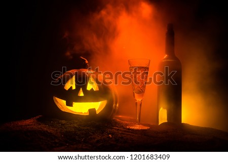 Halloween wine party theme. Glass of wine and bottle with Halloween - old jack-o-lantern on dark toned foggy background. Scary Halloween pumpkin