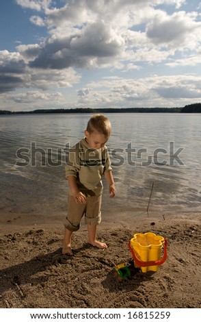 The boy is facing the lake on the beach
