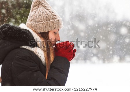 Young Girl in Red Gloves holds a Red Cup with Hot Tea on the Bac