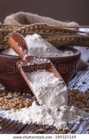Shovel flour with wheat in background on wooden table