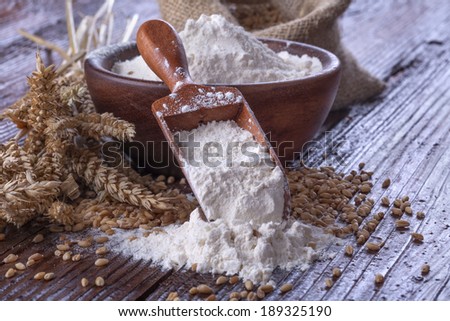 Shovel flour with wheat in background on wooden table