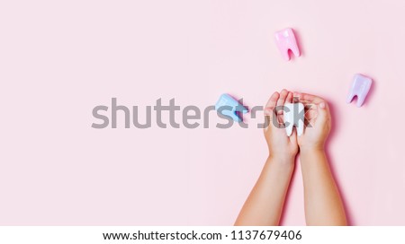 Child\'s hands holding big tooth and toothbrush on pink backgroubd. Healty care teeth concept. Top view, flat lay. Copy space for your text.