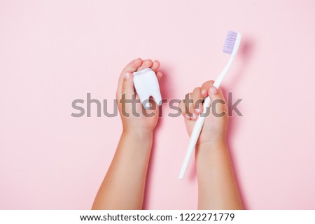 Child\'s hands holding big tooth and toothbrush on pink backgroubd. Healty care teeth concept. Top view, flat lay. Copy space for your text.