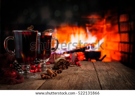 Hot mulled wine in a glass with orange slices, anise and cinnamon sticks on vintage wood table. Fireplace as background. Christmas or winter warming drink.