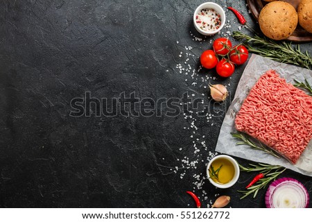 raw minced meat on paper, ingredients for burger with tomato, onion and seasonings on black background top view