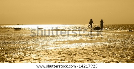 two men with the boat on the shore during sunset. yellow toned.