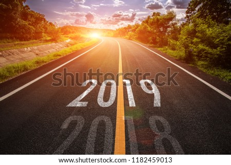 The word 2019 written on highway road in the middle of empty asphalt road at golden sunset and beautiful blue sky. Concept for new year 2019.