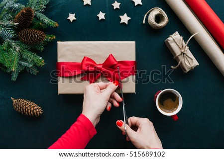 Concept of Christmas items on a table. Woman\'s hands wrapping Christmas gift