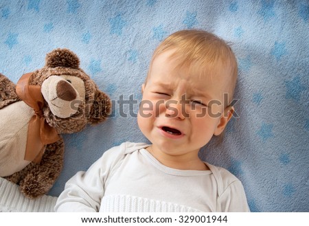 One year old baby crying in bed with a teddy bear