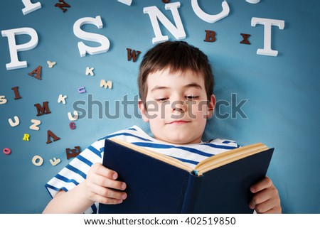 seven years old child lying with book and letters on blue background