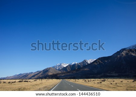 Panorama road to mountain, clear blue sky, yellow field meadow. Winter traveling in New Zea-land