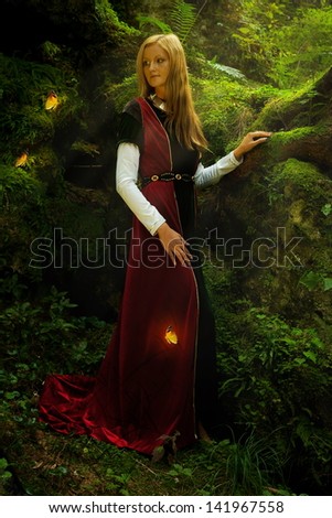 A beautiful woman fairy with long blonde hair in a historical gown is turning her head just to have a glimpse of shining golden butterflies flying around her in the deep woods