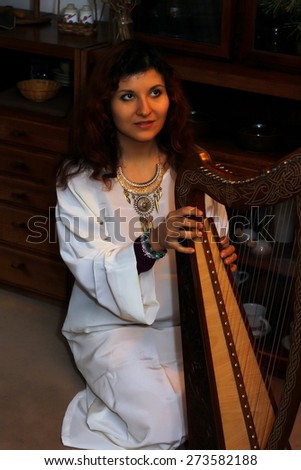Young woman playing celtic harp in a white angelic historical costume