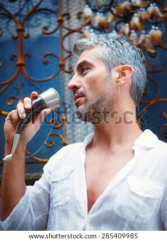 Sexi Man in a white shirt and medieval mead horn in hand. Toast concept. Drunk facial expressions. Ornamental window on background, and Dream Catcher.