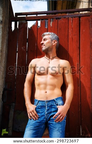 Sexy fashion portrait hot male model in stylish jeans with muscular body posing. Wolves tooth jewelery pendant.