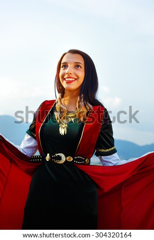 young woman with dark hair, green and red velvet historical dress and gold jewel and a subtle smile