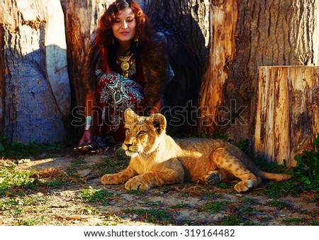 young woman with ornamental dress and gold jewel playing with lion cub in nature