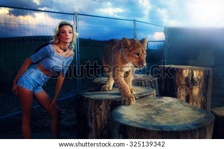 sexy woman playing with lion cub on background with beautiful sky and storm clouds