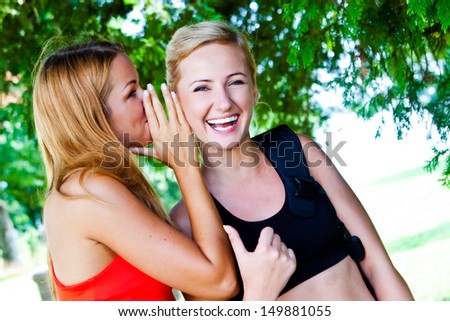 Two happy young girlfriends telling secrets.