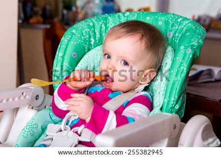Naughty cute baby eating alone in the high chair