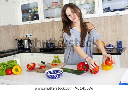 Portrait of a young woman doing a salad in her kitchen, while cooking, happy smile