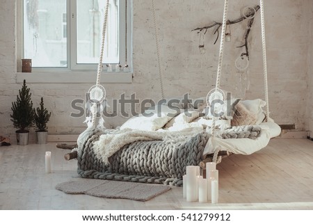The bed suspended from the ceiling. Grey big cozy blanket knit. Scandinavian style, gray plaid, candles.