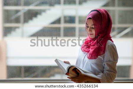 Beautiful Muslim girl reading book with hijab and smiling.