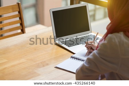 Muslim woman working with computer in the room , writing paper