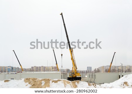 Building site with crane trucks that works on construction in the overcast weather