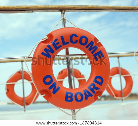 Orange life buoys with welcome on board on it hanging on boat