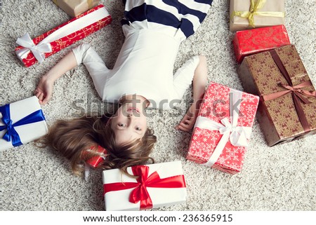 Pretty little girl in a beautiful dress lying on the carpet surrounded by gift boxes. Studio photo