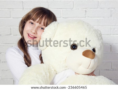 Portrait of a young beautiful girl hugging her big white Teddy bear against white brick wall. Studio photo