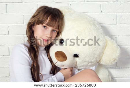 Pretty girl with her big white Teddy bear against white brick wall. Studio photo