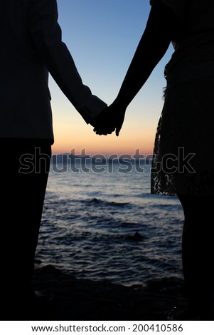 Romantic silhouette couple holding hands on a beach in sunset.