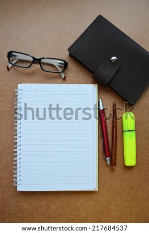 Notebook, red pen, wooden pencil, marker pen, eye glasses on wooden background.