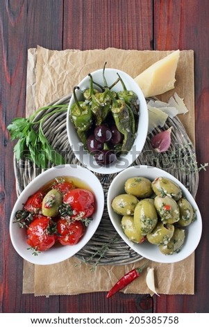 Antipasti:black and green olives,baked cherry tomatoes and roasted pimento on a wooden table. Selective focus.