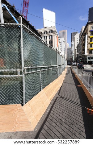 Urban sidewalk screened off from construction site in urban setting. Vertical.