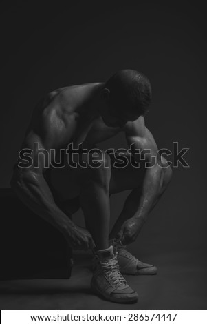 Muscular athlete man tie her shoes, black and white