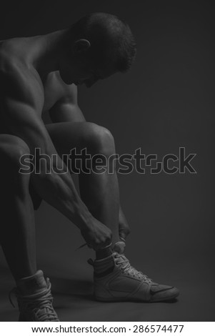 Muscular athlete man tie her shoes, black and white