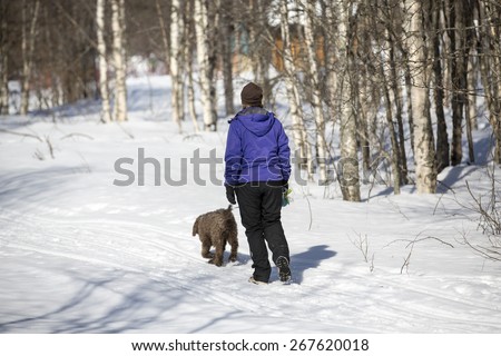 A woman walking the dog in sunshine during the spring. The dog is a lagotto romagnolo