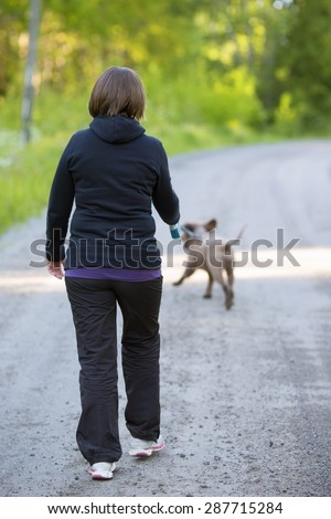 A woman walking the dog on an empty road. The dog is a Lagotto Romagnolo also known as Italian waterdog.