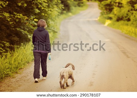 A woman walking the dog on a silent road. Image has a vintage effect. Dog breed is Lagotto romagnolo also known as Italian waterdog.