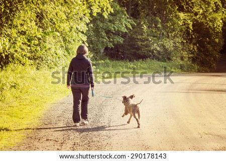 A woman walking the dog on a silent road. Image has a vintage effect. Dog breed is Lagotto romagnolo also known as Italian waterdog.