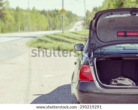 An image of a car trunk open waiting for help in side of the road. Image has a vintage effect.