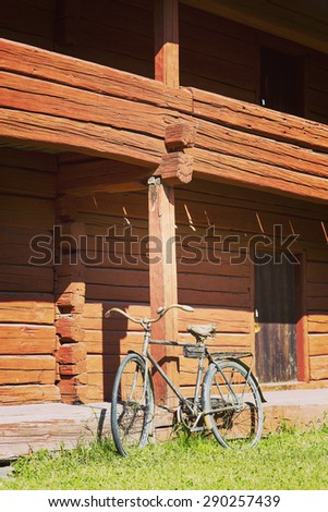 A very old bicycle is parked next to old red barn. Image has a vintage effect.