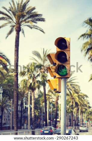 A traffic light showing green next palm trees in the streets of Barcelona.