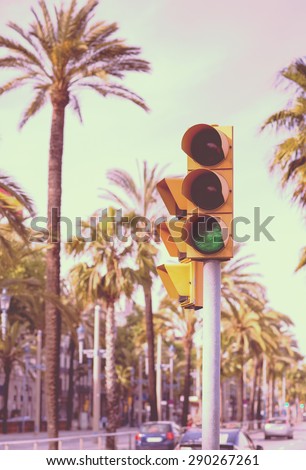 A traffic light showing green next to palm trees in the streets of Barcelona, Spain. Image has a vintage effect.