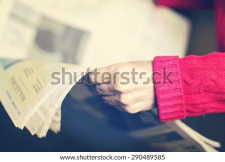 An elderly woman is reading a newspaper. Image has a vintage or hipster effect.