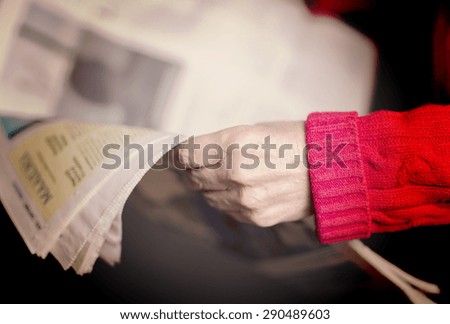 An elderly woman is reading a newspaper. Image has a vintage effect.